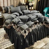 A dark gray bed with a layered duvet and skirt featuring intricate gold lace edging.