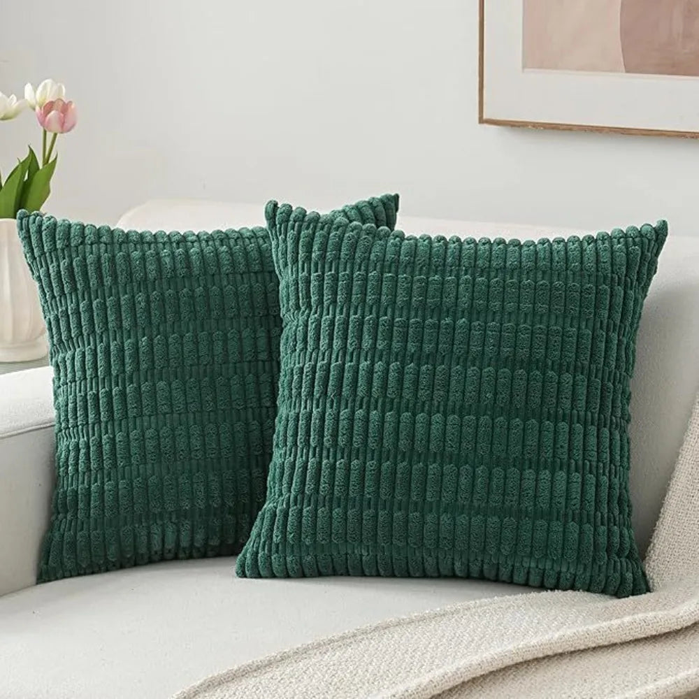 A set of two dark green, textured knit throw pillows resting on a light-colored sofa.