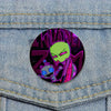 An enamel pin featuring a green, menacing alien character with purple accents and the text Invader ZIM.
