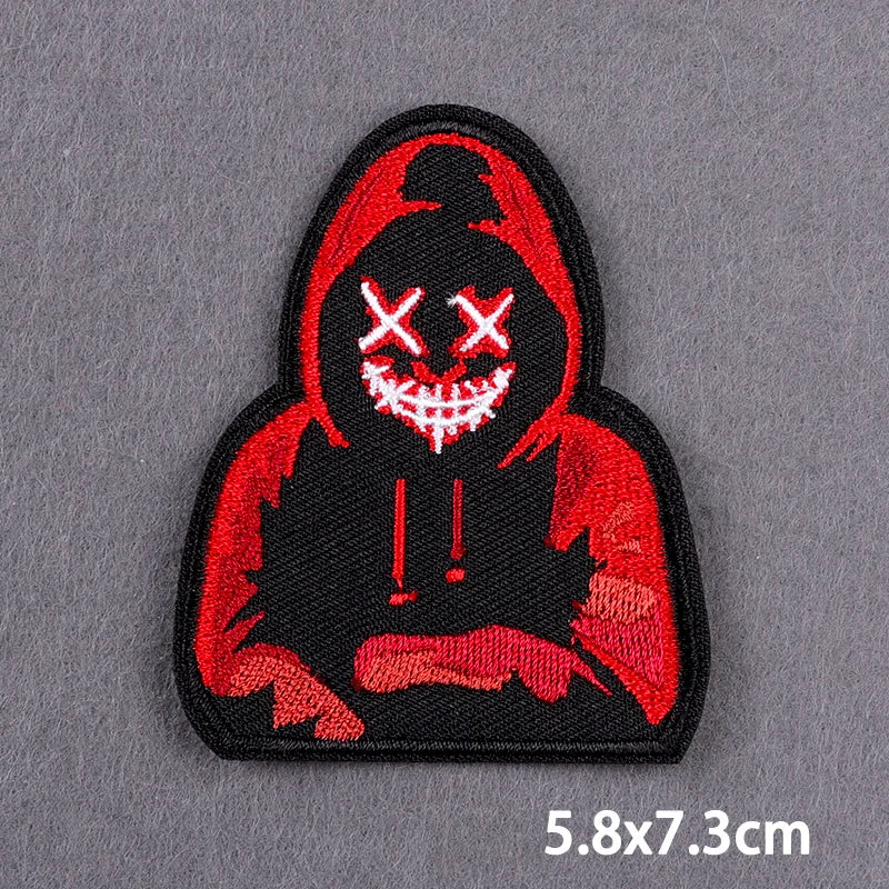 A black embroidery patch featuring a red hooded figure with white crossed eyes and stitched details.