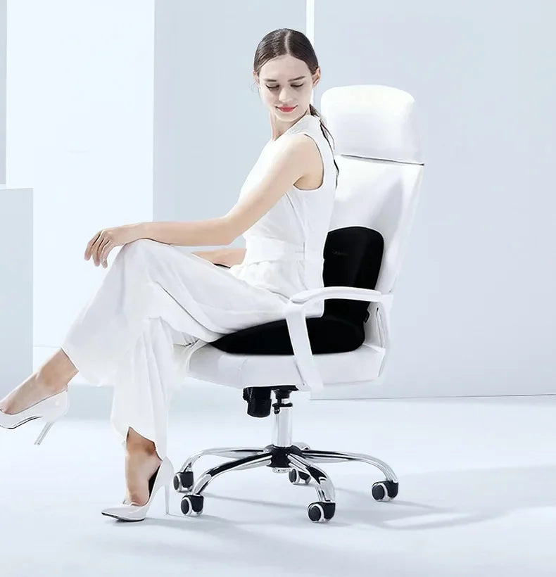A woman sits in a white ergonomic chair with black padding, wearing white pants and heels.