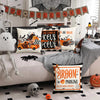 A set of four Halloween cushion covers featuring ghost, pumpkin, and skull designs displayed on a sofa.