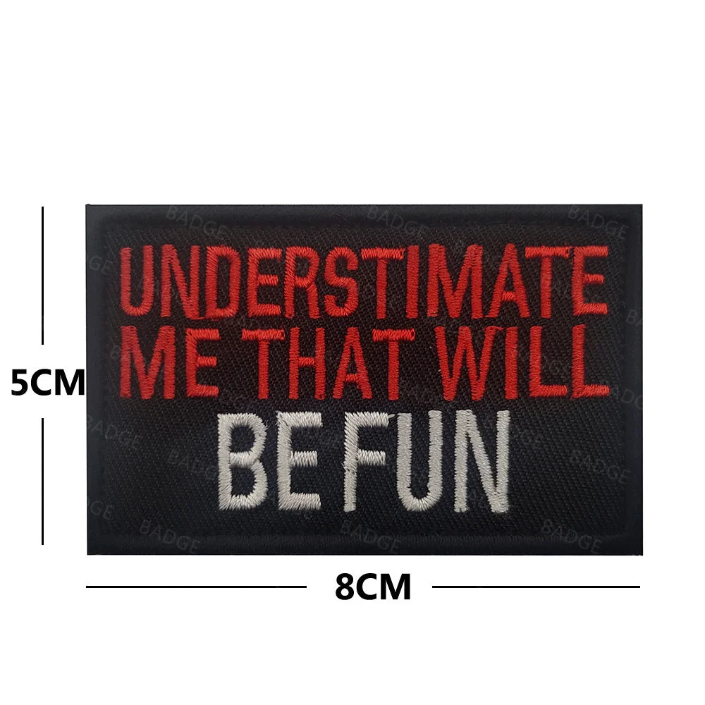Black embroidered patch with white text that reads UNDERESTIMATE ME THAT WILL BE FUN