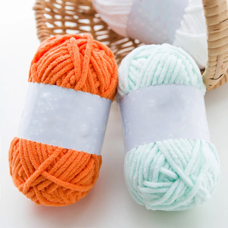Two skeins of thick orange and mint green velvet yarn are displayed on a woven tray.