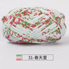 A ball of hand-dyed fabric strip yarn featuring a white background with pink and green patterns.