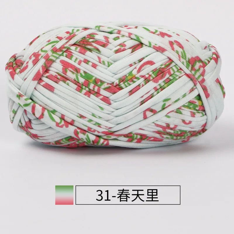 A ball of hand-dyed fabric strip yarn featuring a white background with pink and green patterns.