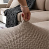A hand is adjusting a beige woven fabric cover on a sofa, showing the texture and fit of the stretchy polar fleece.