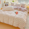 A light pink floral printed bedding set with white embroidery and pillows on a bed.