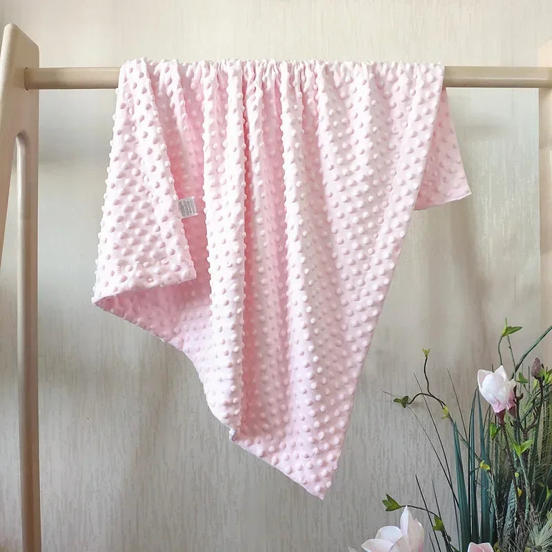 Pink fleece swaddle blanket with a quilted texture hanging on a wooden rack.