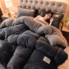 A person relaxing under a large, dark gray plush fleece blanket on a bed.