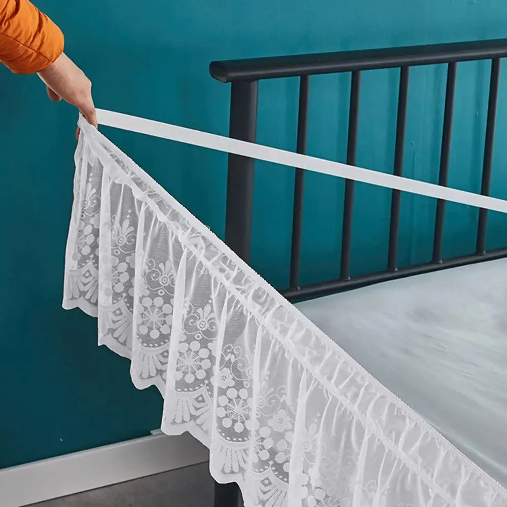 White lace ruffle bed skirt hanging over a dark metal bed railing against a teal wall.