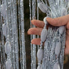 A hand is holding a vertical string curtain made of silver beads and gray fabric for a doorway or wedding decor.