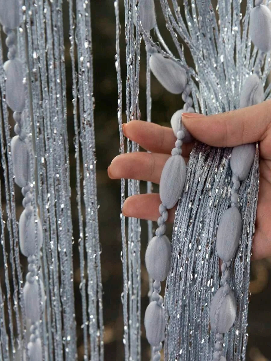 A hand is holding a vertical string curtain made of silver beads and gray fabric for a doorway or wedding decor.