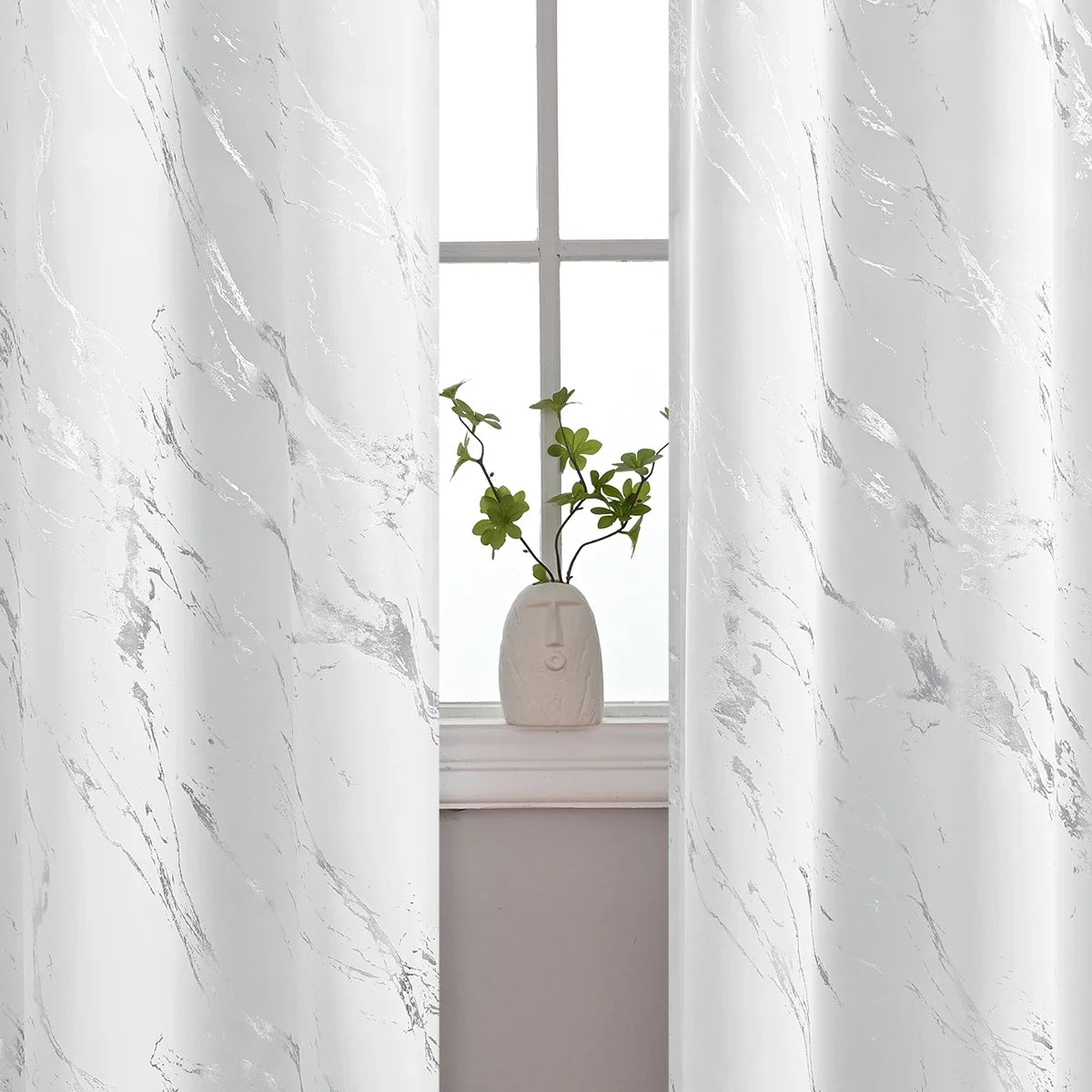 White marble printed curtain panels framing a window with a small green plant.