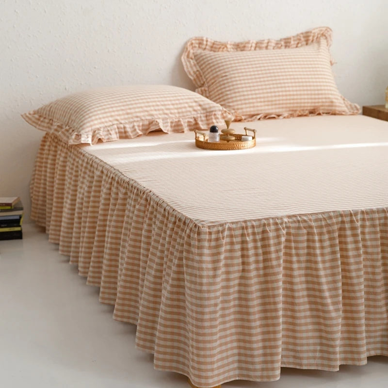 A beige plaid cotton bed skirt cover with ruffled edges and matching pillow covers on a bed.