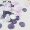 A collection of silk rose petals in shades of purple, lavender, and white scattered on a white surface.
