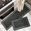 A set of black diatom mud floor mats with the word HOME embossed on them placed on a white countertop.