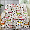 A patterned flannel blanket featuring various dachshund silhouettes in pink, brown, yellow, and green on a white background.