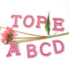 Pink pearl rhinestone letter patches spelling out the alphabet A through E for DIY projects