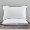 A white luxury goose down and feather bed pillow with brown piping resting on a gray fabric.
