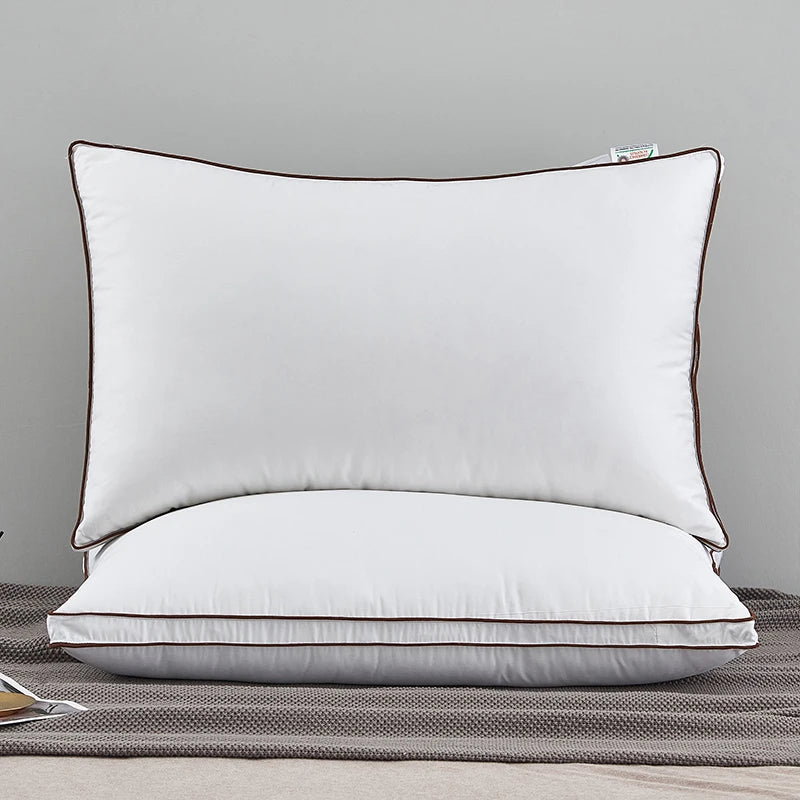 A white luxury goose down and feather bed pillow with brown piping resting on a gray fabric.
