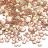 A close-up view of a mix of rose gold and champagne colored clear glass rhinestones for DIY crafts.