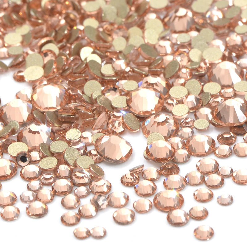 A close-up view of a mix of rose gold and champagne colored clear glass rhinestones for DIY crafts.