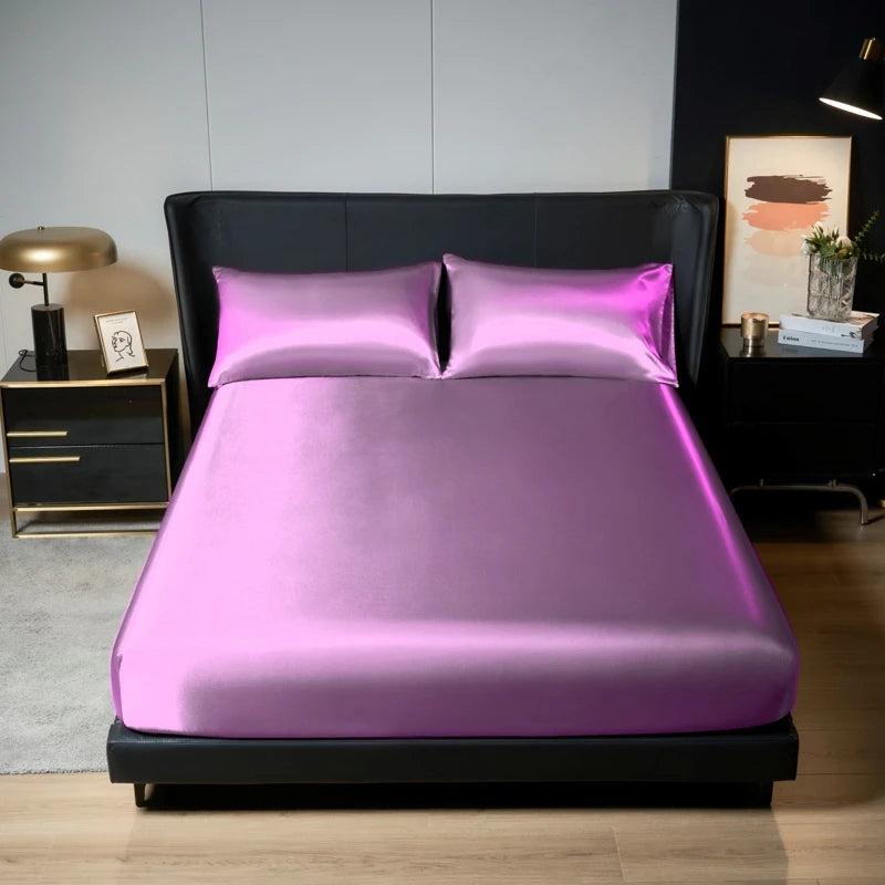 A vibrant pink satin bedding set featuring a fitted sheet and pillowcases displayed on a black bed frame.