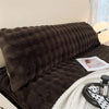 A dark brown plush long pillowcase resting on a bed, next to a white knitted blanket.