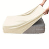 A hand is draping a cream-colored velvet stretchy sofa seat cover over a gray sofa cushion.