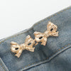 Gold-toned adjustable waist clip brooches pinned onto a denim fabric.