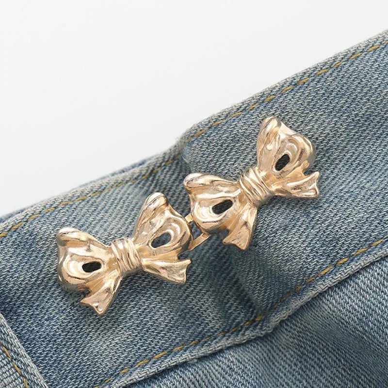 Gold-toned adjustable waist clip brooches pinned onto a denim fabric.