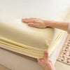 A hand is folding a light yellow fitted bed sheet on a white mattress.