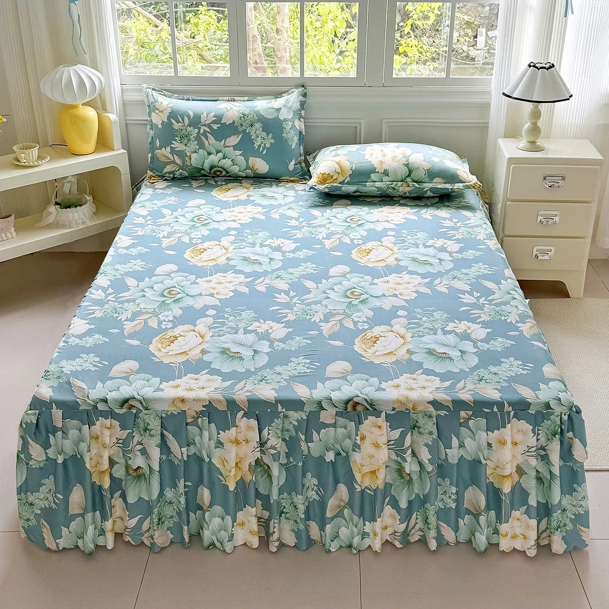 A bed set featuring a blue floral print skirt, pillows, and bedding displayed in a bright room.