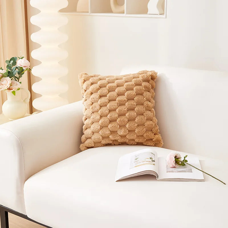 A textured, brown plush pillow resting on a white sofa next to an open book.