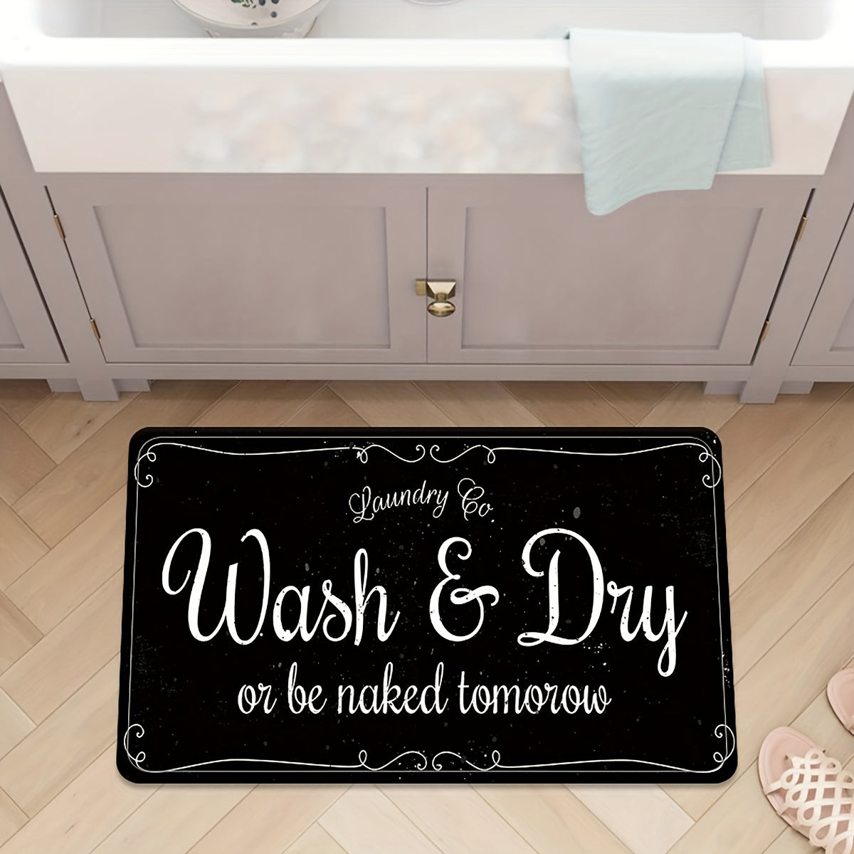 A black laundry mat with white text that reads Wash & Dry or be naked tomorrow placed on a wooden floor.
