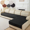 A beige sofa with black quilted anti-slip cushion covers and decorative round fabric accents.
