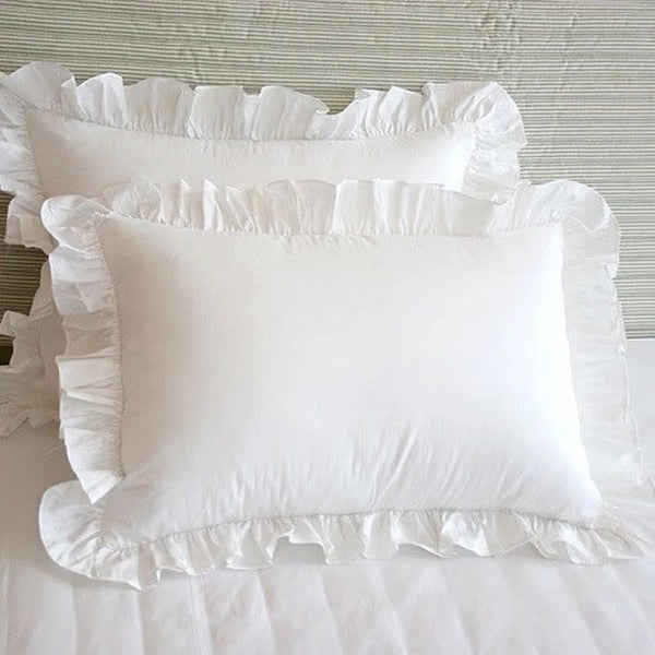 A set of two white minimalist ruffle pillow covers displayed on a white bed.