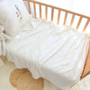 A white fleece swaddle blanket with a dotted pattern is displayed on a wooden crib railing.
