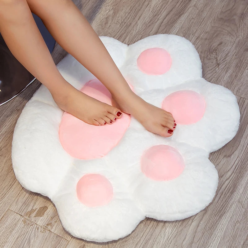 A white plush bear paw cushion with pink accents is shown being used by a person's foot.
