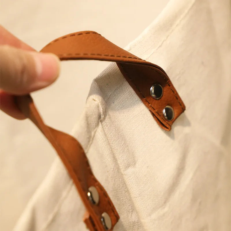 A hand is holding a brown leather strap with metal rivets, showing a detail of a folding cartoon printed storage basket for b