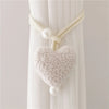 White plush heart tiebacks with pearl accents used to tie back a sheer white curtain.