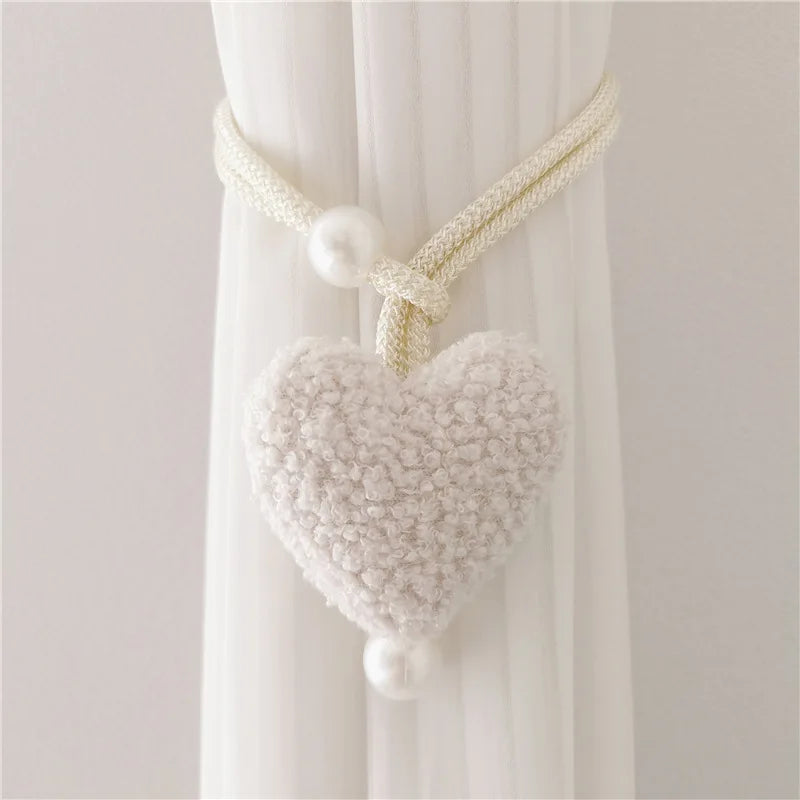 White plush heart tiebacks with pearl accents used to tie back a sheer white curtain.