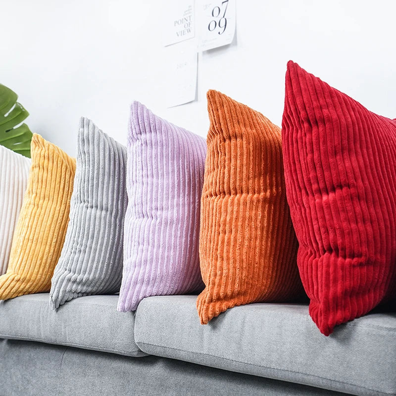 A row of textured corduroy cushion covers in shades of yellow, gray, lavender, orange, and red displayed on a sofa.