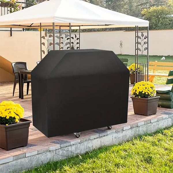 A black heavy-duty BBQ grill cover is placed on a brick patio next to potted yellow flowers.