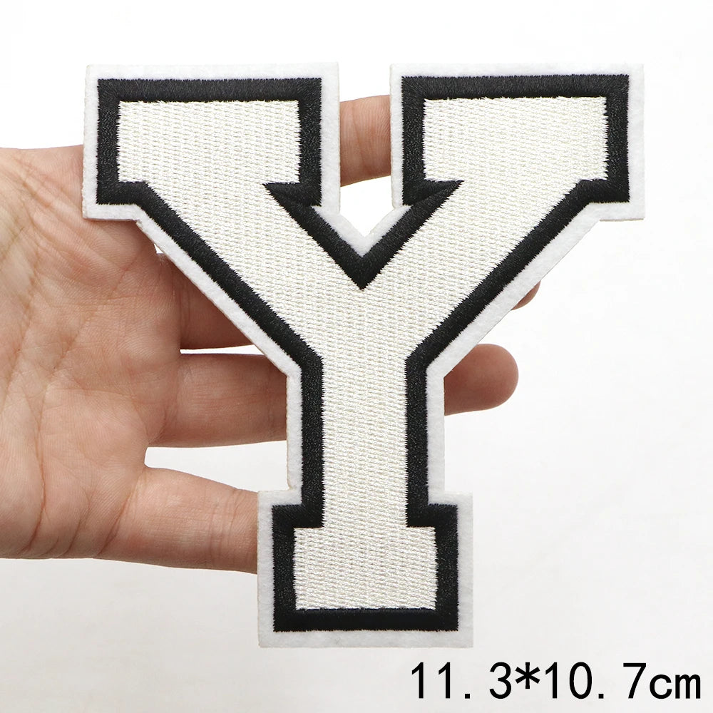 A hand holds a large letter Y patch with black and white stitching.