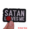 Black embroidered patch with white text Satan Loves Me on a fabric background