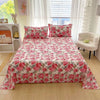 Red floral print flat bed sheets for double beds with pink pillows on a light wood floor.