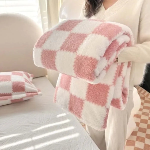A pink and white checkered fluffy blanket is held by a person in a white sweater.