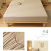 A beige fitted bed sheet set displayed on a wooden bed frame with natural light and decorative elements.